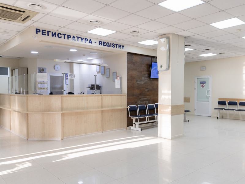 Просторный светлый холл с регистратурой в центре и рядами кресел вдоль стен
